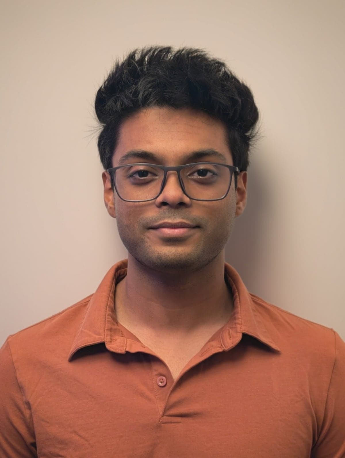 Aditya Aryan: glasses, a rust polo shirt, a plain background.